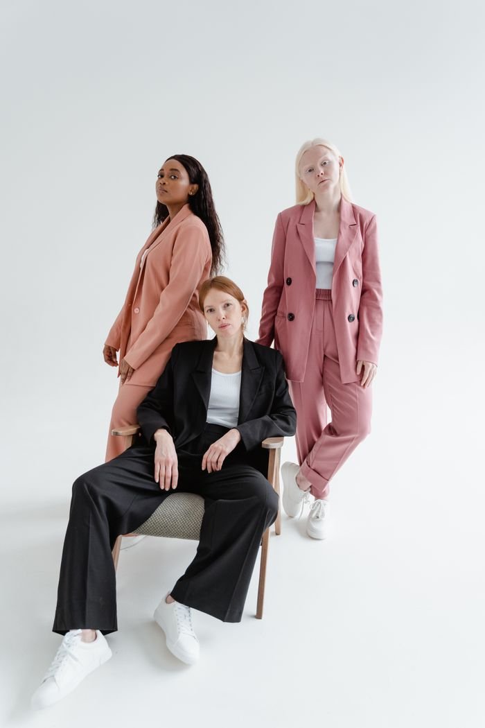 Services Three stylish women in blazers posing confidently in a bright studio setting.
